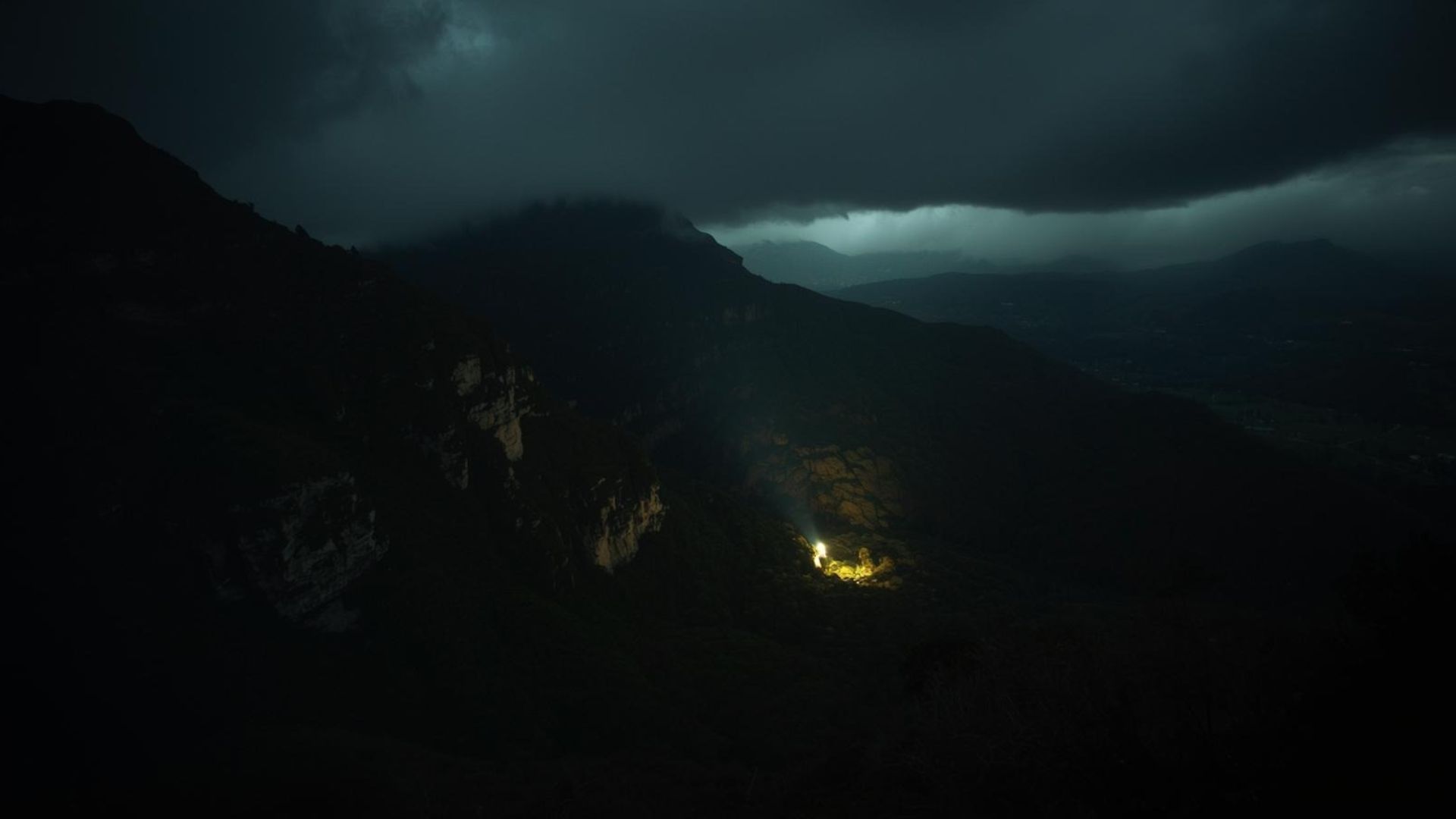 Storm clouds rolling over high cliffs, a single light below